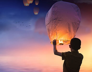 person holding floating lantern under sunset thumbnail