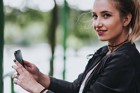 Blonde woman in a black jacket and ripped jeans by a green handrail thumbnail