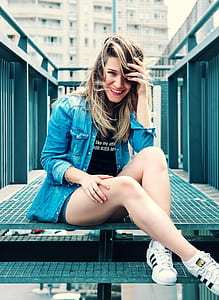 woman wearing blue denim jacket sitting on stairs in front of white building thumbnail