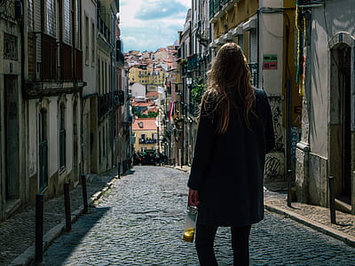 Woman in Black Coat Standing in Pathway Between Commercial Buildings thumbnail