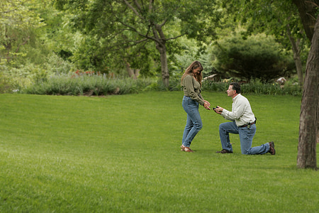 man kneeling in front of woman on green grass field thumbnail