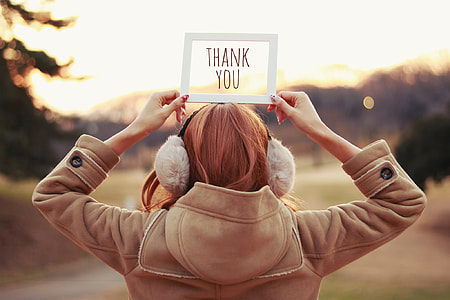 selective focus photography of woman wearing brown hoodie jacket holding Thank You signage during golden hour thumbnail