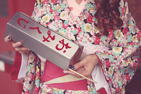 woman in white, black and red floral traditional dress holding foreign script box thumbnail