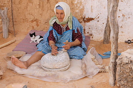 woman wearing blue and white gingham dress sitting next to black and white cat in front of gray rock during daytime thumbnail