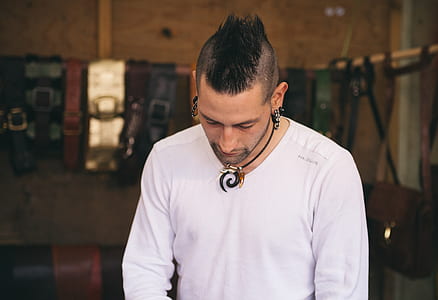 man wearing white V-neck long-sleeved shirt looking down near bags hanging on rods inside well lit room thumbnail