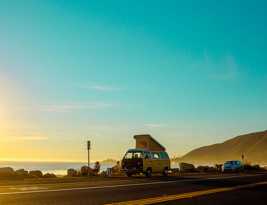 yellow van parked on roadside near body of water thumbnail