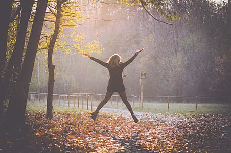woman jumping on withered leaves under trees thumbnail