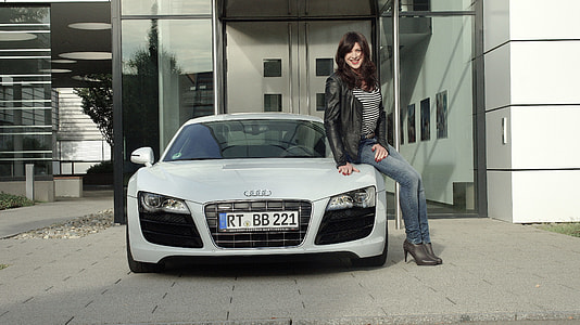 woman in black jacket sitting on Audi A7 hood beside white high rise building thumbnail