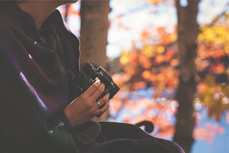 close-up photography of person holding black binoculars near trees thumbnail