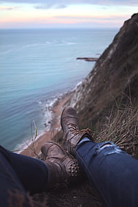 selective focus photography of person wearing pair of gray leather side-zipped combat boots sitting on edge of mountain by the sea thumbnail