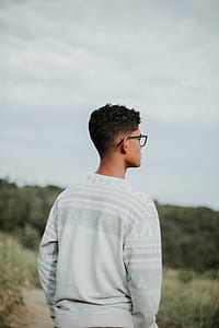 man wearing white and grey crew-neck sweater standing on the grass field during daytime thumbnail
