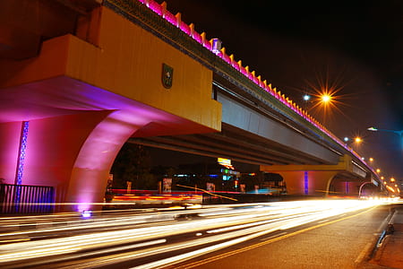 timelapse photography of vehicle travelling on road below bridge at night time thumbnail