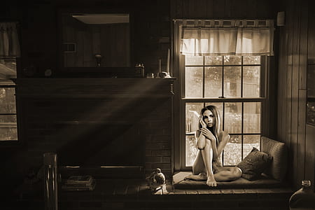 grayscale photo of woman sitting on sofa near window thumbnail