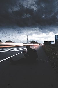time lapse photography of man sitting on pave road under cumulus clouds thumbnail