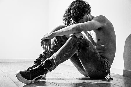 greyscale photo of topless man sitting on floor near wall inside room thumbnail