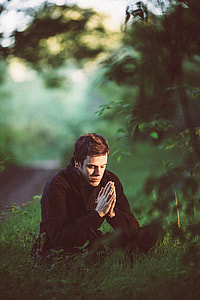 man in black coat sitting on grass near trees thumbnail