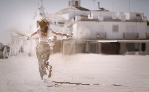 Woman Running on Sand Near White Concrete Building thumbnail