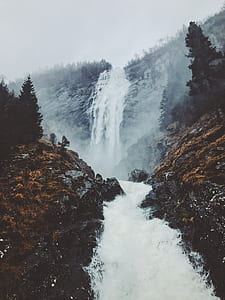 waterfalls flowing in between rocks and mountain during daytime thumbnail