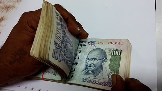 person holding 100 Indian rupee banknote bundle thumbnail