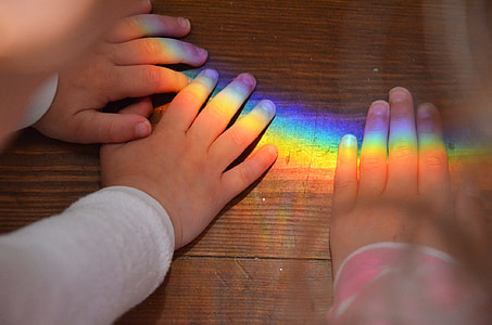 three person's hands placed on brown wooden surface with rainbow colored light thumbnail