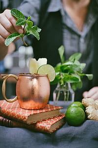 person holding mint leaf on top of bronze-colored mug thumbnail