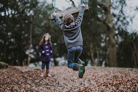 child in gray long-sleeved shirt hanging on brown wooden swing near trees during daytime thumbnail