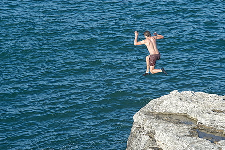 photo of man that jumps on cliff near body of water thumbnail