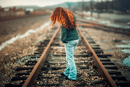 red-haired female standing on railway during daytime thumbnail