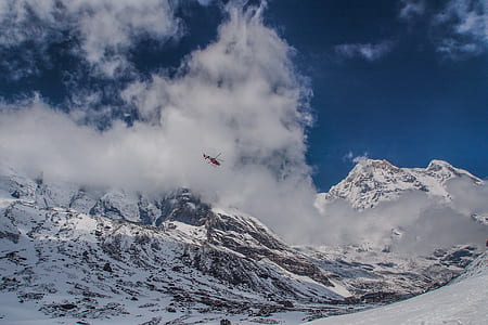 red helicopter flying around over snowcap mountain thumbnail