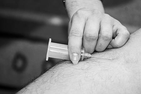 grayscale photo of syringe needle near human skin thumbnail