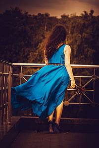 woman wearing blue sleeveless dress and black heels standing beside gray metal railings thumbnail