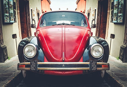 red Volkswagen Beetle coupe park between buildings thumbnail