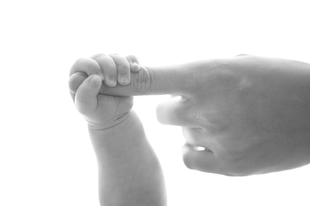 toddler and parent holding finger in greyscale photography thumbnail