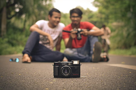 black camera in front of two men sitting on road thumbnail
