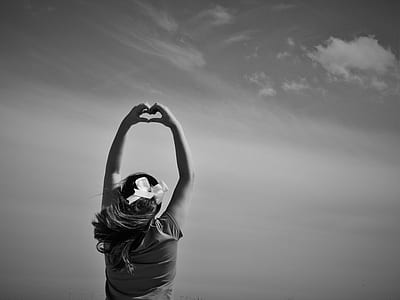 grayscale photo of person wearing cap-sleeved top with hands on air doing heart shape during daytime thumbnail