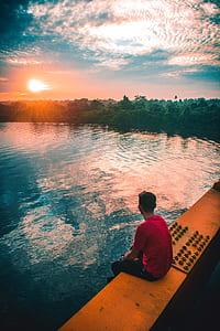 man sitting on rail above body of water thumbnail