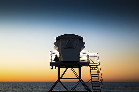 person sitting on lifeguard shed near body of water thumbnail