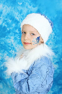 girl wearing blue floral faux-fur jacket and white knit cap with blue face paint thumbnail