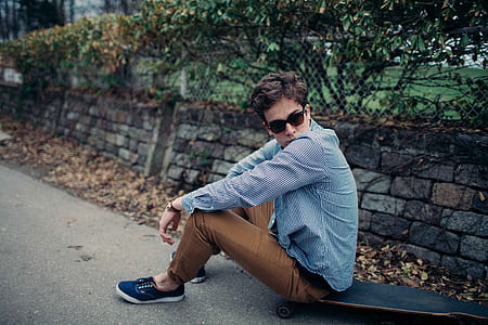 man sitting on black longboard near wall during daytime thumbnail