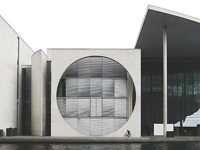 person riding on bike beside white concrete building during daytime thumbnail
