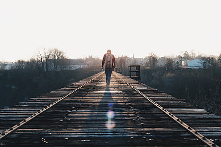 man carrying backpack while walking along wooden road thumbnail
