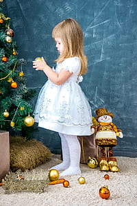 girl in white and light-blue dress holding gold-colored Christmas bauble thumbnail