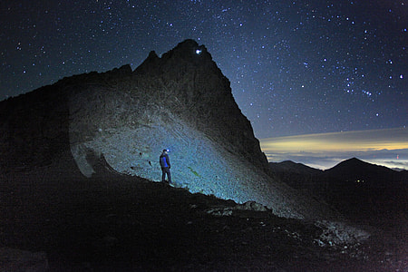 man in blue jacket standing near mountain at nighttime thumbnail