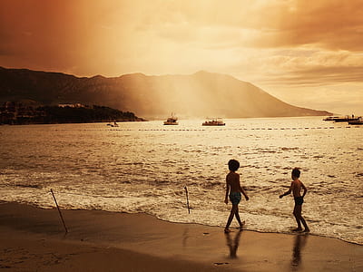 two children standing on shore during golden hour thumbnail