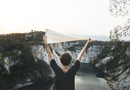 woman raising white flaglet in front of body of water thumbnail