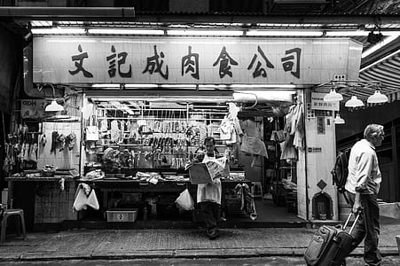 grayscale photography of man walking with trolley bag on front of store thumbnail