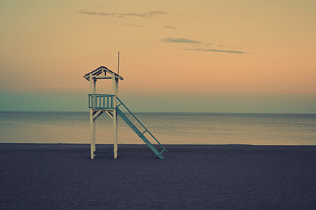 photo of white and blue wooden tower beside beach under gray sky thumbnail