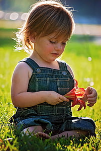 girl in blue overall pants holding red lily flower thumbnail