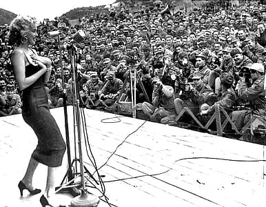 greyscale photo of woman in dress performing in front soldiers thumbnail