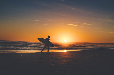 silhouette of man carrying surfboard beside seashore during sunset thumbnail